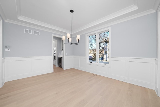 unfurnished dining area with an inviting chandelier, crown molding, a raised ceiling, and light wood-type flooring