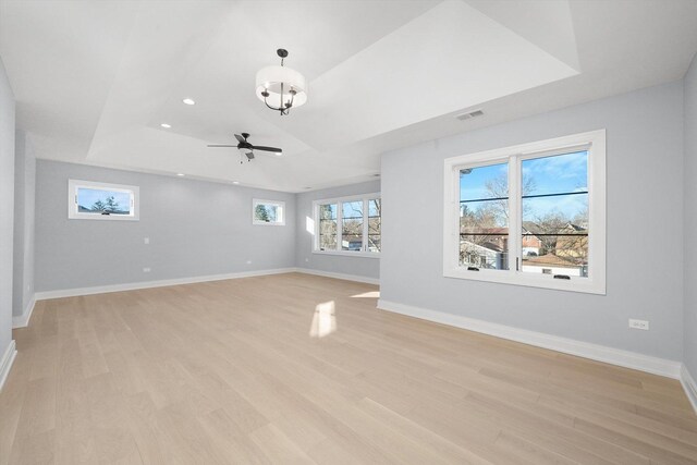 unfurnished living room featuring ceiling fan with notable chandelier, light hardwood / wood-style floors, and a raised ceiling