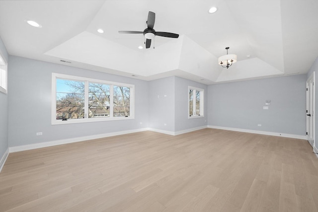 unfurnished living room with ceiling fan with notable chandelier, a wealth of natural light, light hardwood / wood-style floors, and a raised ceiling