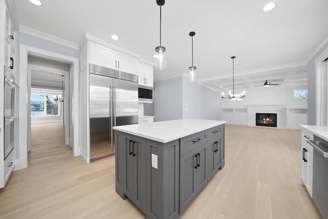 kitchen with white cabinetry, gray cabinetry, a center island, built in appliances, and light stone counters