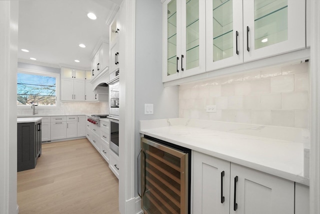 kitchen with white cabinets, beverage cooler, decorative backsplash, light stone countertops, and light hardwood / wood-style flooring