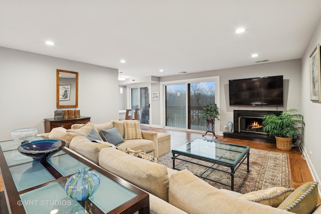 living area with a warm lit fireplace, wood finished floors, and recessed lighting