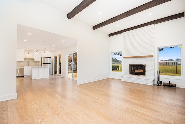 unfurnished living room with beam ceiling, sink, a brick fireplace, and light hardwood / wood-style flooring