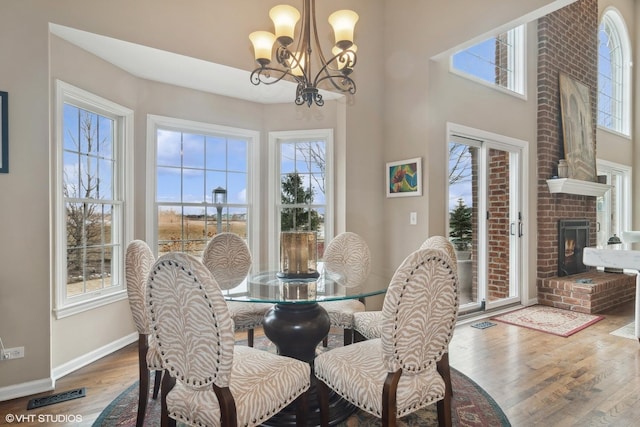 dining space featuring a brick fireplace, a wealth of natural light, wood-type flooring, and a chandelier