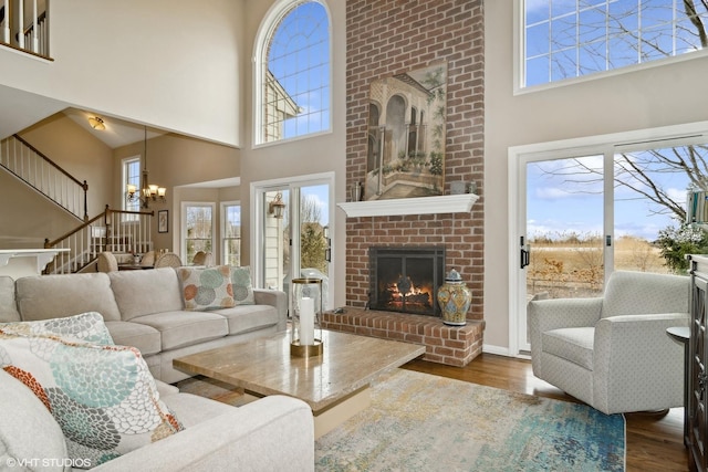 living room featuring dark wood-type flooring, an inviting chandelier, a brick fireplace, and a high ceiling