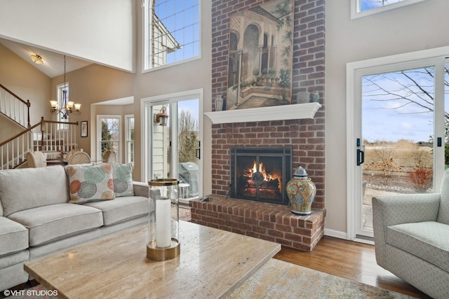 living room featuring hardwood / wood-style floors, a towering ceiling, a chandelier, and a brick fireplace