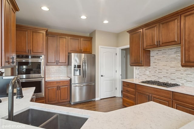 kitchen with sink, stainless steel appliances, dark hardwood / wood-style floors, light stone counters, and decorative backsplash