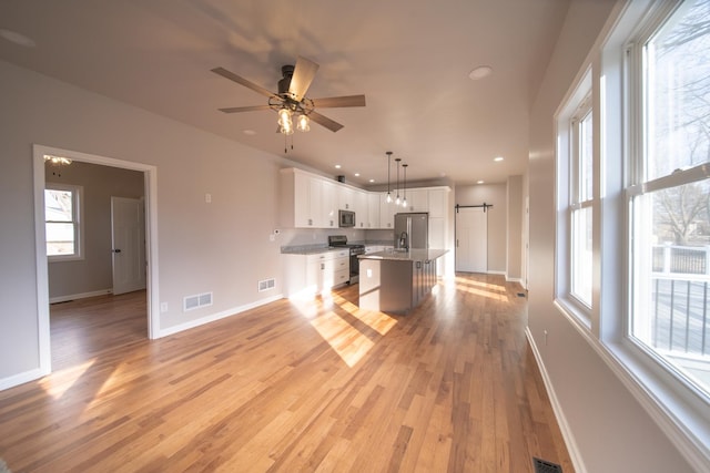 kitchen with a breakfast bar, a kitchen island with sink, stainless steel appliances, white cabinets, and decorative light fixtures