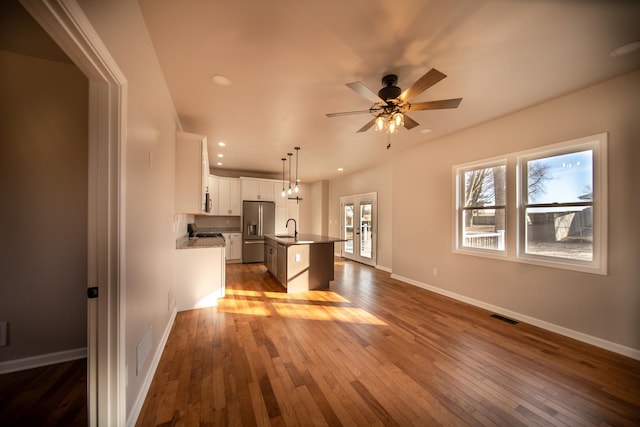 kitchen with pendant lighting, white cabinetry, sink, stainless steel fridge with ice dispenser, and a center island with sink