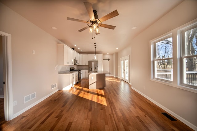 kitchen with dark wood-type flooring, white cabinetry, hanging light fixtures, stainless steel appliances, and a center island with sink