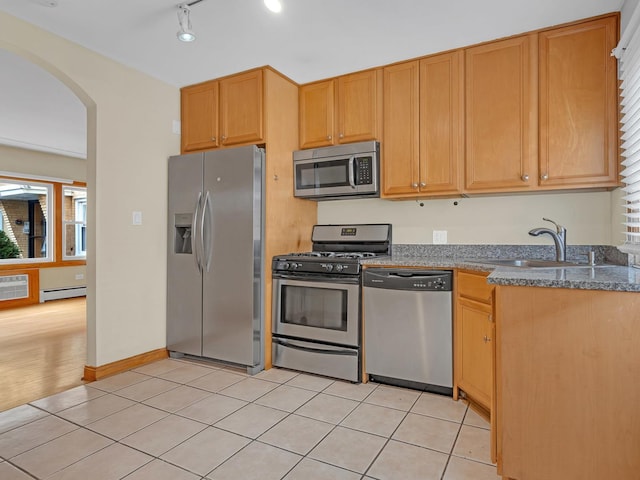 kitchen with sink, stone countertops, light tile patterned floors, appliances with stainless steel finishes, and a baseboard heating unit