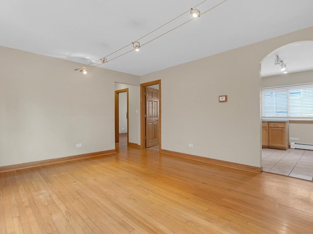 empty room with track lighting, light hardwood / wood-style floors, and baseboard heating