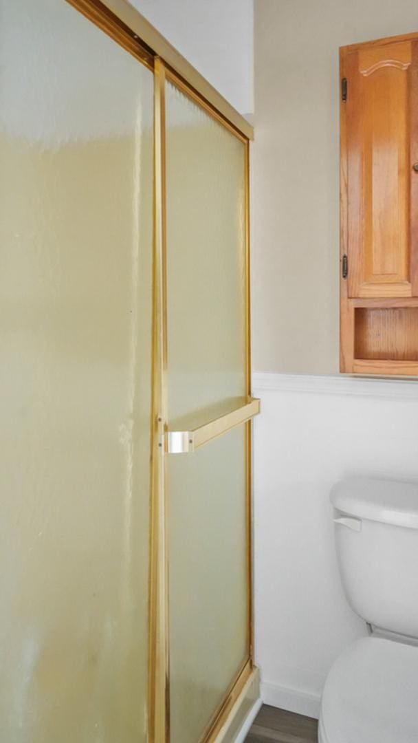 bathroom featuring wood-type flooring, toilet, and a shower with door