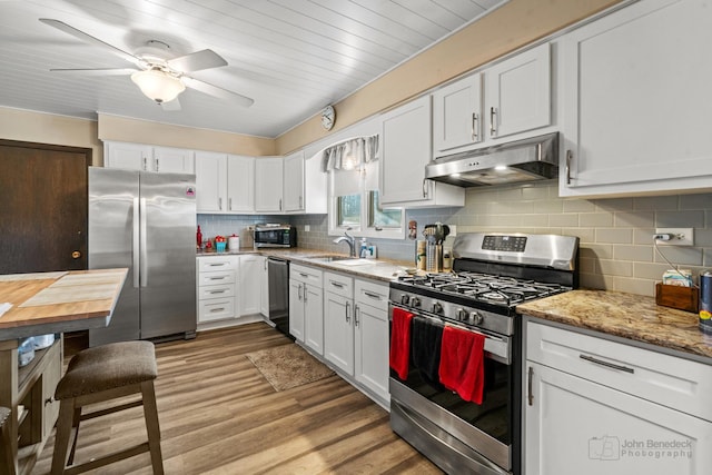 kitchen featuring sink, white cabinetry, light wood-type flooring, appliances with stainless steel finishes, and light stone countertops