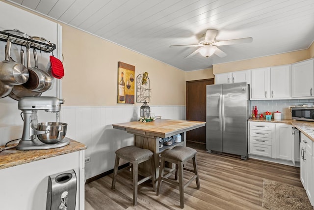 kitchen with appliances with stainless steel finishes, light stone counters, white cabinets, and light wood-type flooring