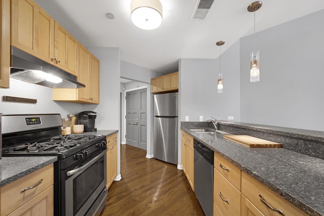 kitchen featuring dark wood-type flooring, light brown cabinetry, decorative light fixtures, appliances with stainless steel finishes, and dark stone counters