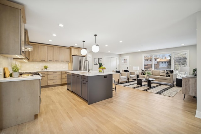 kitchen with decorative light fixtures, backsplash, stainless steel fridge, a kitchen island with sink, and light wood-type flooring