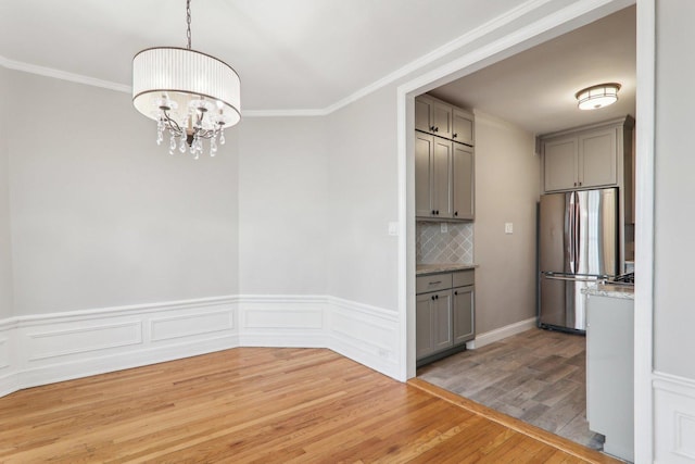 unfurnished dining area featuring crown molding, hardwood / wood-style floors, and a notable chandelier