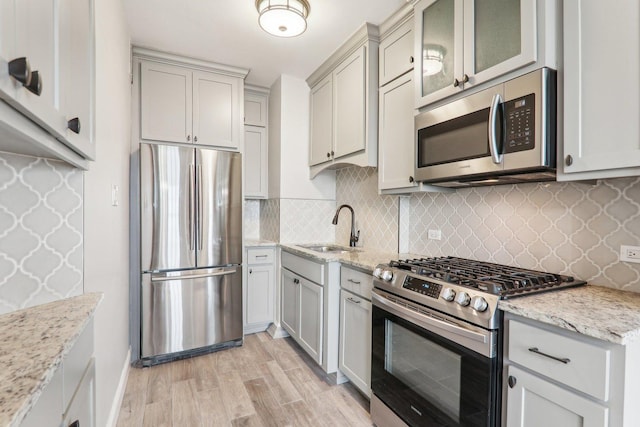 kitchen featuring stainless steel appliances, light stone countertops, sink, and light wood-type flooring