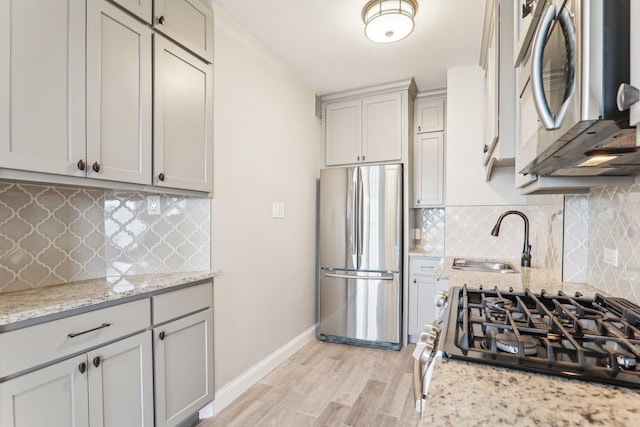 kitchen with appliances with stainless steel finishes, light stone countertops, sink, and gray cabinetry