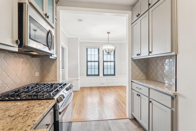 kitchen featuring decorative light fixtures, ornamental molding, light hardwood / wood-style floors, stainless steel appliances, and light stone countertops