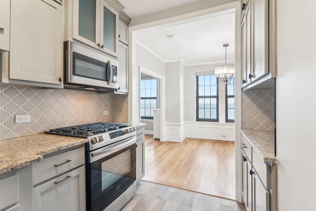 kitchen with light hardwood / wood-style flooring, appliances with stainless steel finishes, hanging light fixtures, light stone countertops, and ornamental molding