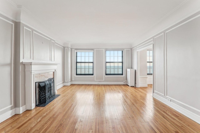 unfurnished living room with light hardwood / wood-style flooring, radiator, a fireplace, and ornamental molding