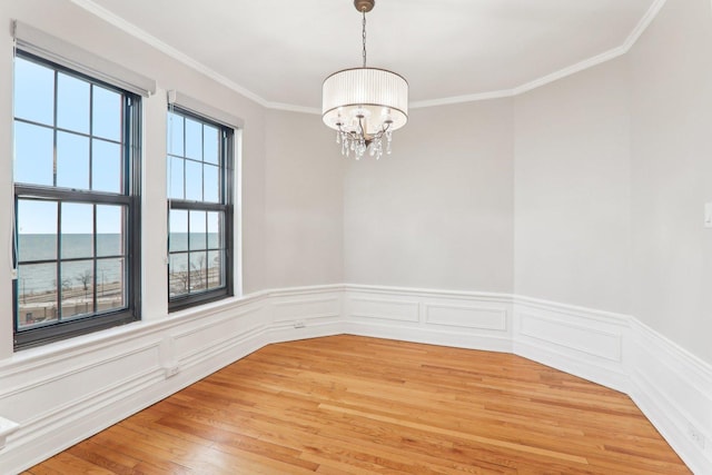 empty room with hardwood / wood-style flooring, crown molding, a water view, and a chandelier