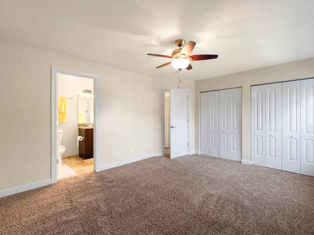 unfurnished bedroom with two closets, light colored carpet, connected bathroom, and ceiling fan