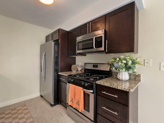 kitchen featuring dark brown cabinetry, appliances with stainless steel finishes, light tile patterned floors, and light stone counters