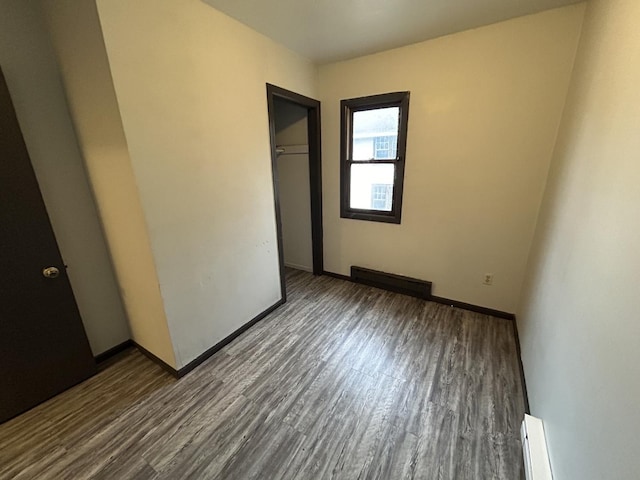 unfurnished bedroom featuring a baseboard radiator, hardwood / wood-style floors, and a closet