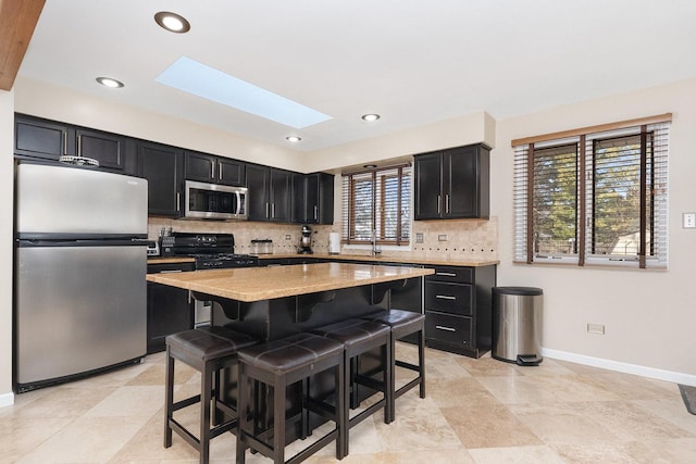 kitchen with a breakfast bar area, light stone counters, a skylight, stainless steel appliances, and backsplash