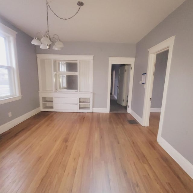 unfurnished living room with a chandelier and light wood-type flooring