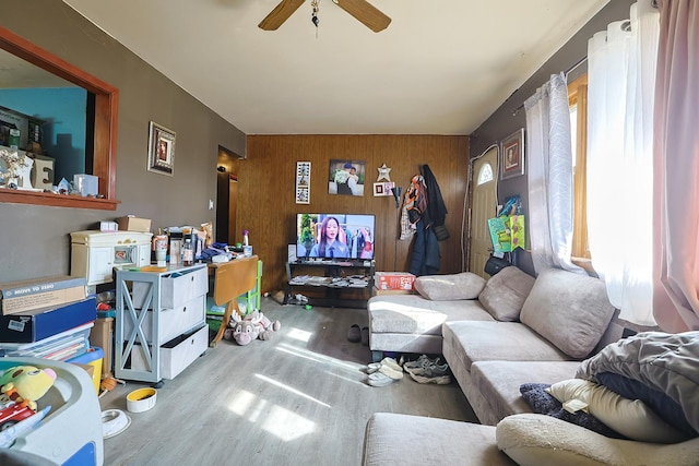 living room with ceiling fan, wood-type flooring, and wooden walls