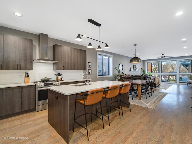 kitchen with stainless steel range with gas cooktop, sink, hanging light fixtures, a kitchen island with sink, and wall chimney range hood