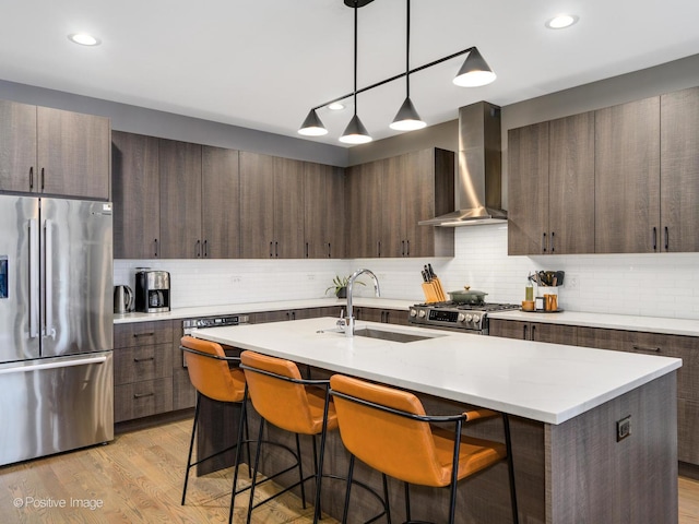 kitchen featuring sink, dark brown cabinets, stainless steel appliances, a kitchen island with sink, and wall chimney range hood