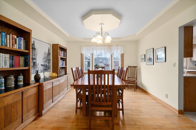 dining space featuring an inviting chandelier, a tray ceiling, and light wood-type flooring