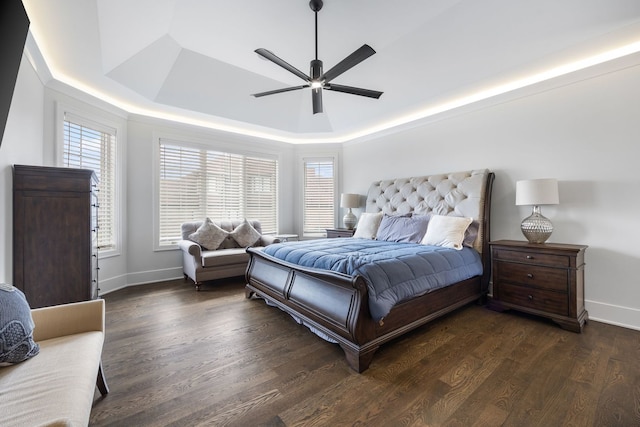 bedroom featuring a raised ceiling, dark wood-type flooring, and ceiling fan