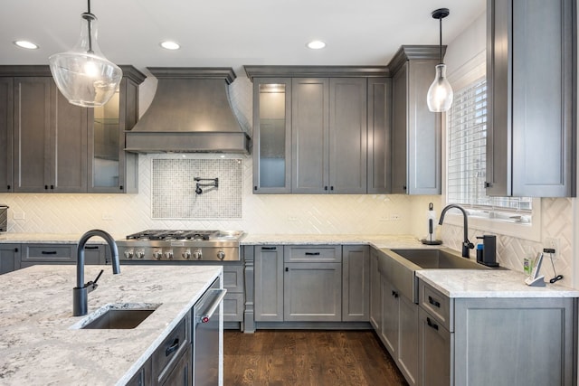 kitchen with light stone counters, decorative light fixtures, sink, and custom exhaust hood