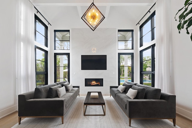 living room featuring baseboards, a towering ceiling, an inviting chandelier, light wood-style floors, and a fireplace