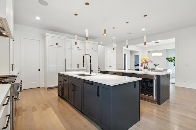 kitchen featuring high end stove, beverage cooler, a sink, light countertops, and a center island with sink