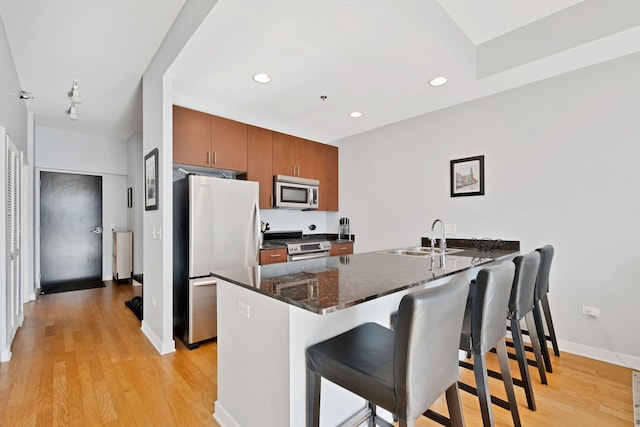 kitchen with sink, dark stone countertops, a kitchen breakfast bar, stainless steel appliances, and light hardwood / wood-style flooring