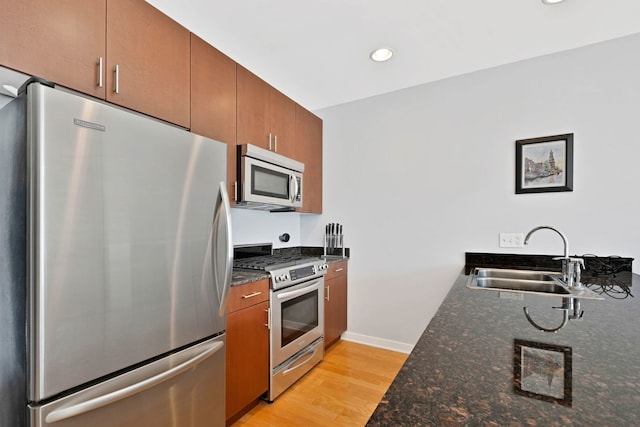 kitchen featuring dark stone countertops, sink, light hardwood / wood-style floors, and appliances with stainless steel finishes