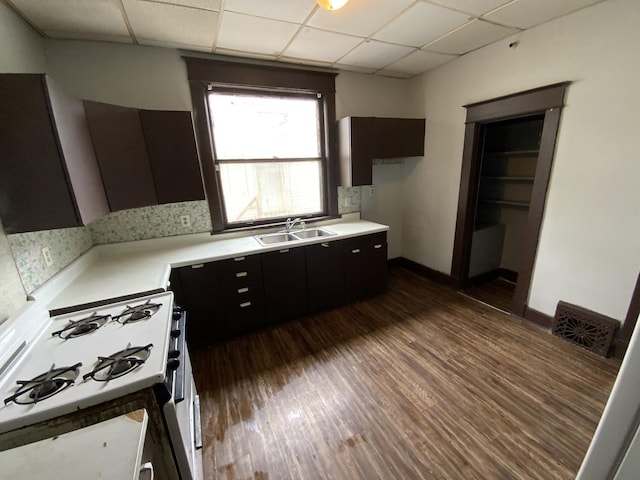 kitchen with dark brown cabinetry, white gas stove, sink, dark hardwood / wood-style floors, and a drop ceiling