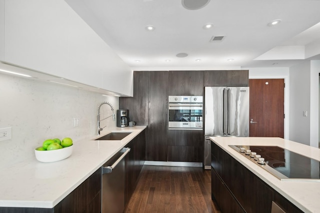 kitchen with sink, light stone counters, dark hardwood / wood-style floors, stainless steel appliances, and decorative backsplash