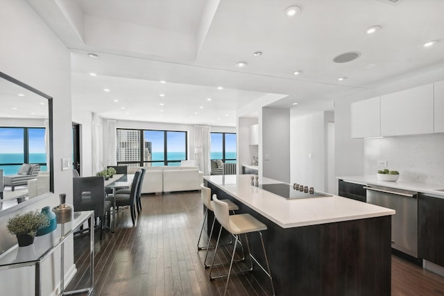 kitchen with a kitchen island with sink, a water view, white cabinets, black electric cooktop, and stainless steel dishwasher