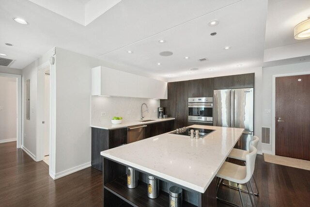 kitchen with dark brown cabinetry, dark hardwood / wood-style flooring, stainless steel appliances, a kitchen island with sink, and white cabinets