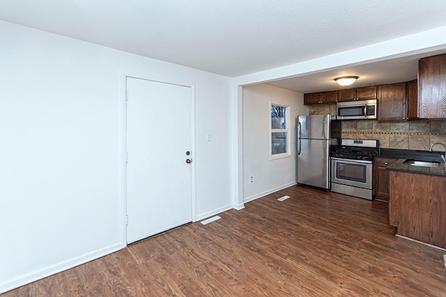 kitchen featuring sink, backsplash, dark hardwood / wood-style flooring, stainless steel appliances, and a textured ceiling