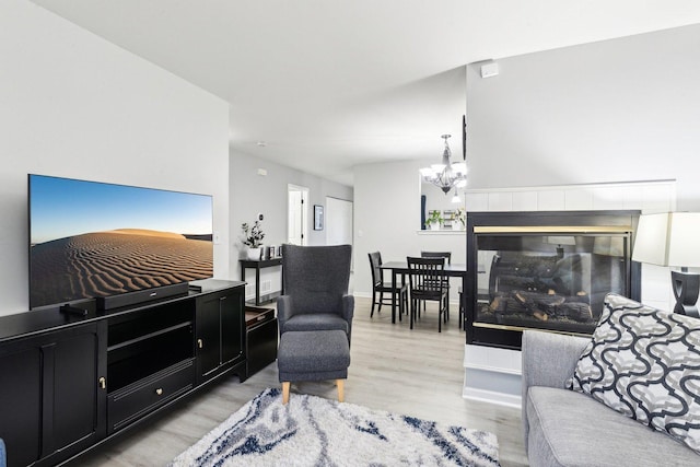 living room with a tiled fireplace, a notable chandelier, and light hardwood / wood-style floors