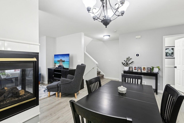 dining room with a multi sided fireplace, light hardwood / wood-style flooring, and a notable chandelier